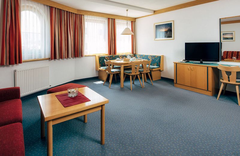 Wohnraum eines Appartements mit roter Sitzgruppe, Essecke und Fernseher